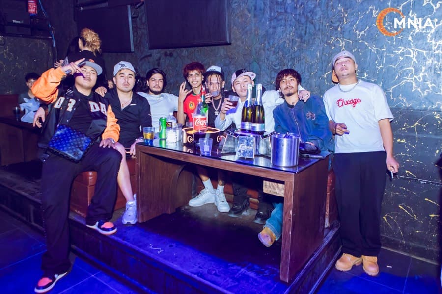 A group at their VIP table against the gold-veined marble wall, bottles and ice buckets out