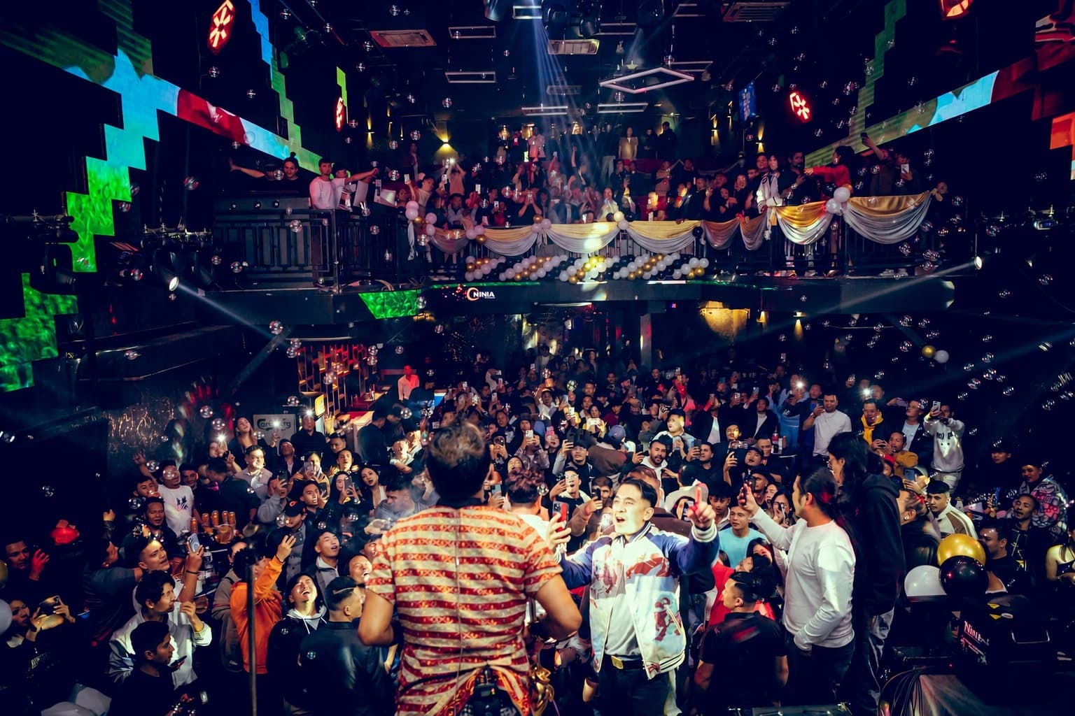 A performer facing a packed floor at OMNIA with the mezzanine balcony full above