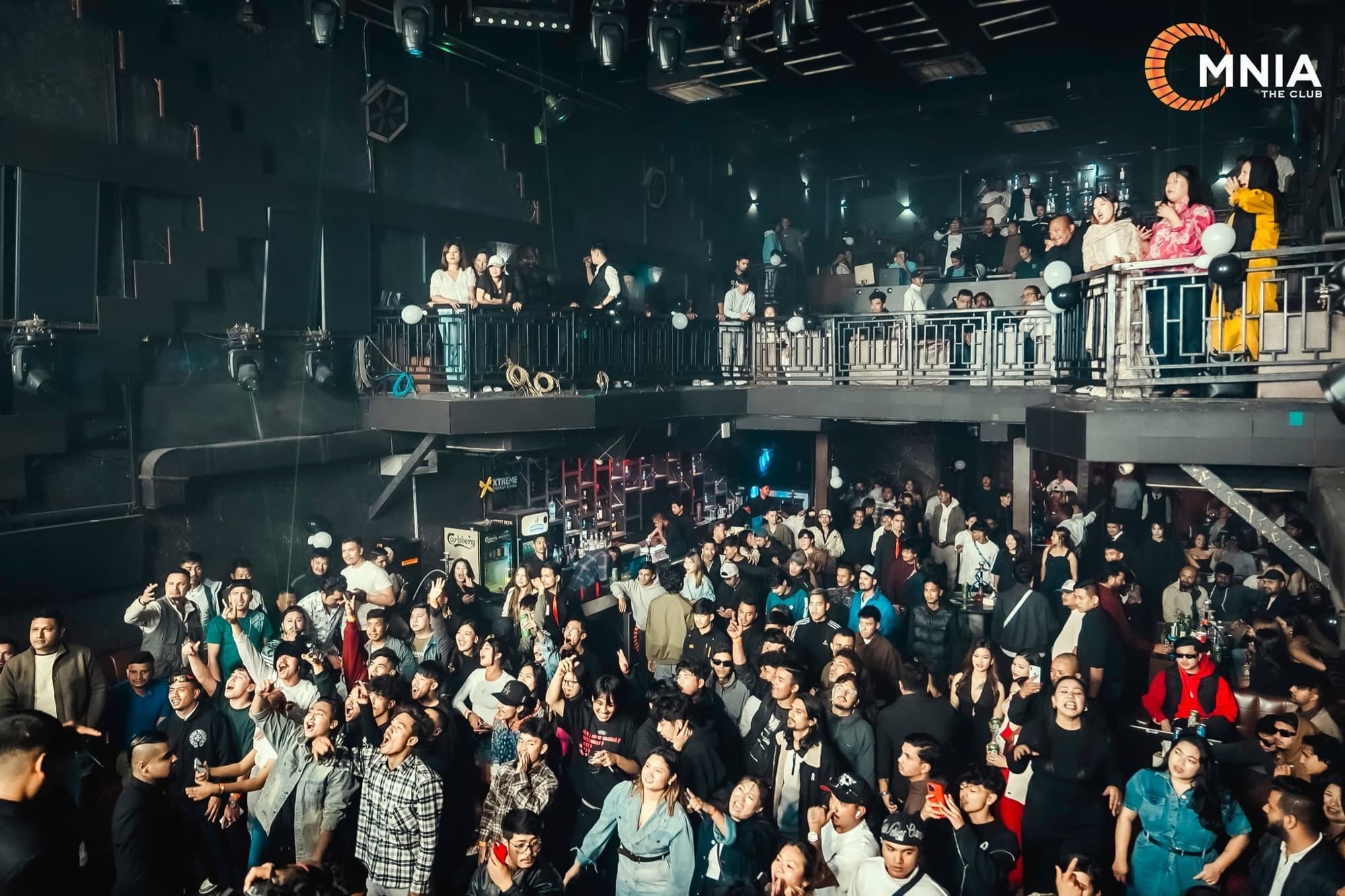 Both levels of OMNIA at once — guests along the mezzanine rail above a packed dance floor